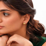 Load image into Gallery viewer, A close-up of a woman wearing a small gold stud earring with a central white inlay, shown against a plain white background.

